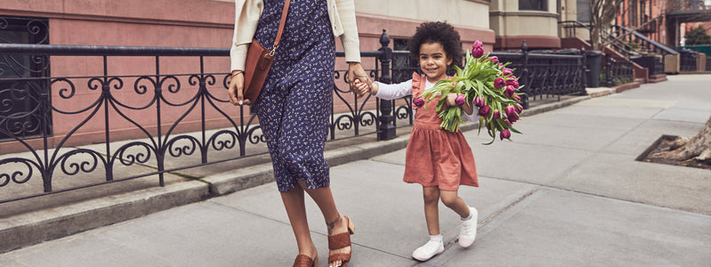 Young girl holding flowers for Mother's Day 2022 and holding her mom's hand.