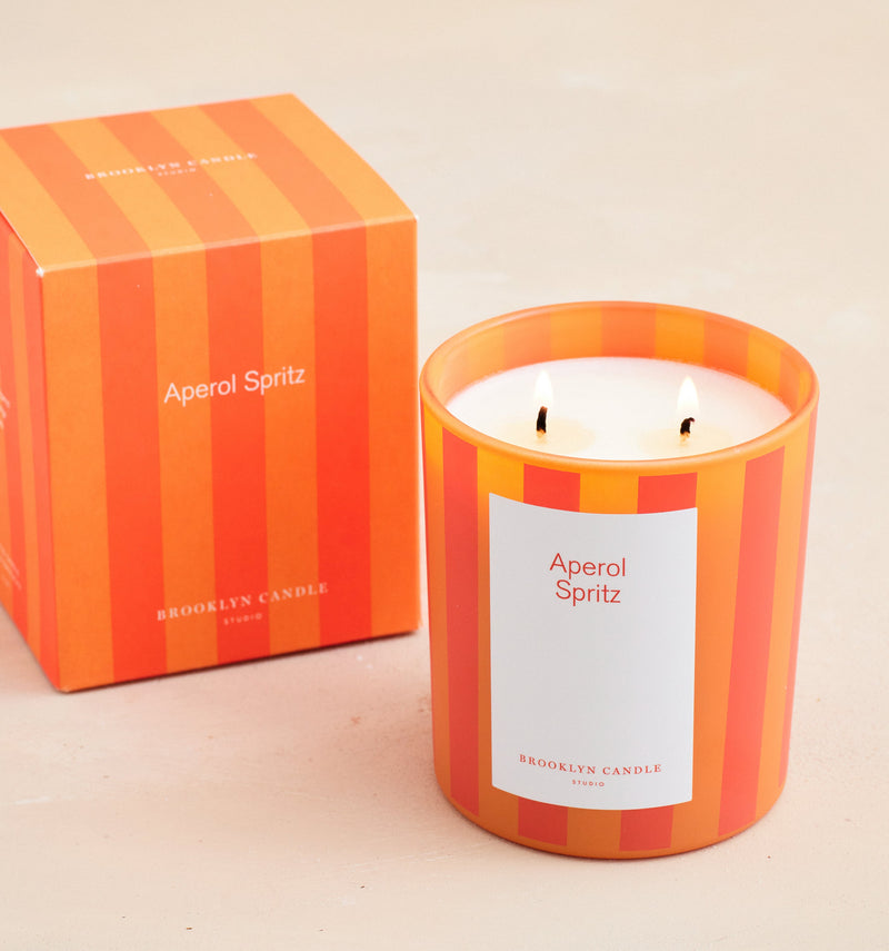 Candle with 'Aperol Spritz' label and matching striped box on a beige background