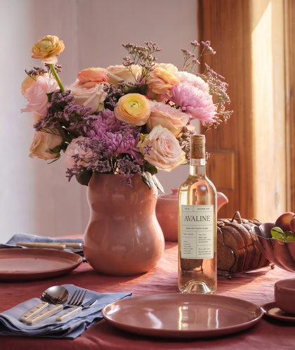 Table setting with a vase of flowers, bottle of wine, and plates.