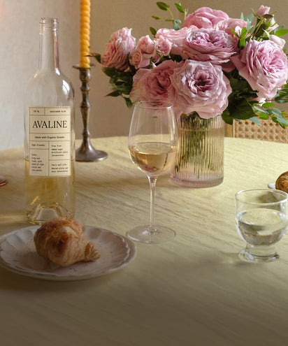 Table setting with Avaline wine bottle, glass of wine, plate with bread, and bouquet of pink roses.