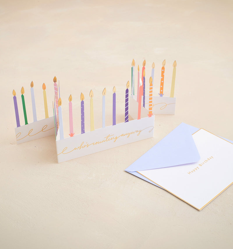 Greeting card with colorful candles and an envelope on a beige background