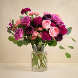 Bouquet of pink and purple flowers in a clear vase on a beige background