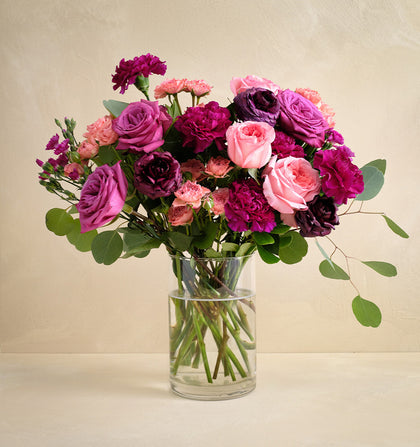 Bouquet of pink and purple flowers in a clear vase on a beige background