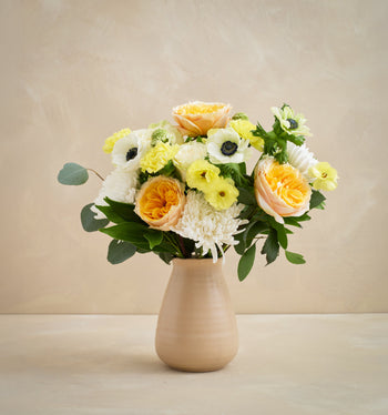 Bouquet of flowers in a beige vase on a wooden surface with a beige background