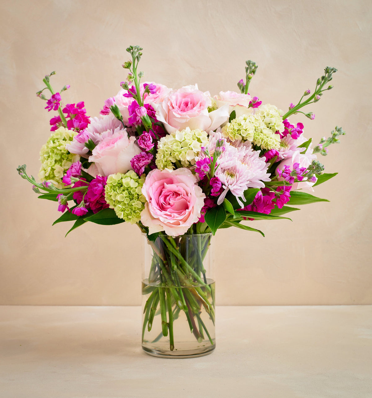 Bouquet of pink and green flowers in a clear vase on a beige background