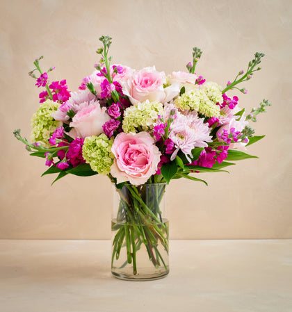 Bouquet of pink and green flowers in a clear vase on a beige background