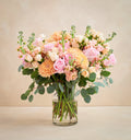 Bouquet of pink and orange flowers in a clear vase on a beige background