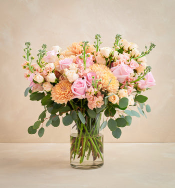 Bouquet of pink and orange flowers in a clear vase on a beige background