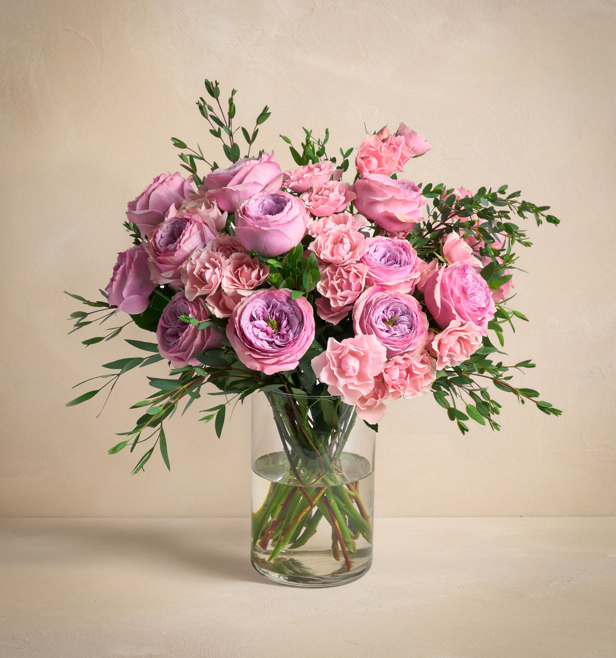 Bouquet of pink and purple flowers in a clear vase on a beige background