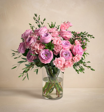Bouquet of pink and purple flowers in a clear vase on a beige background