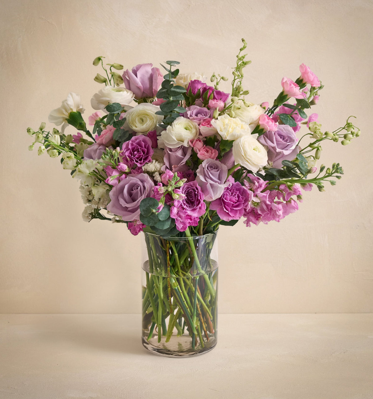 Bouquet of pink, purple, and white flowers in a clear vase on a beige background
