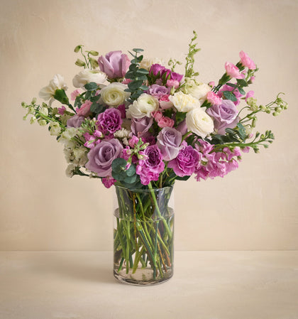 Bouquet of pink, purple, and white flowers in a clear vase on a beige background