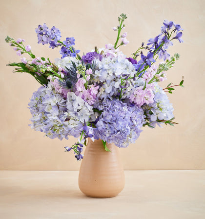 Bouquet of purple and white flowers in a beige vase on a beige background