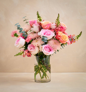 Bouquet of pink and white flowers in a clear vase on a beige background