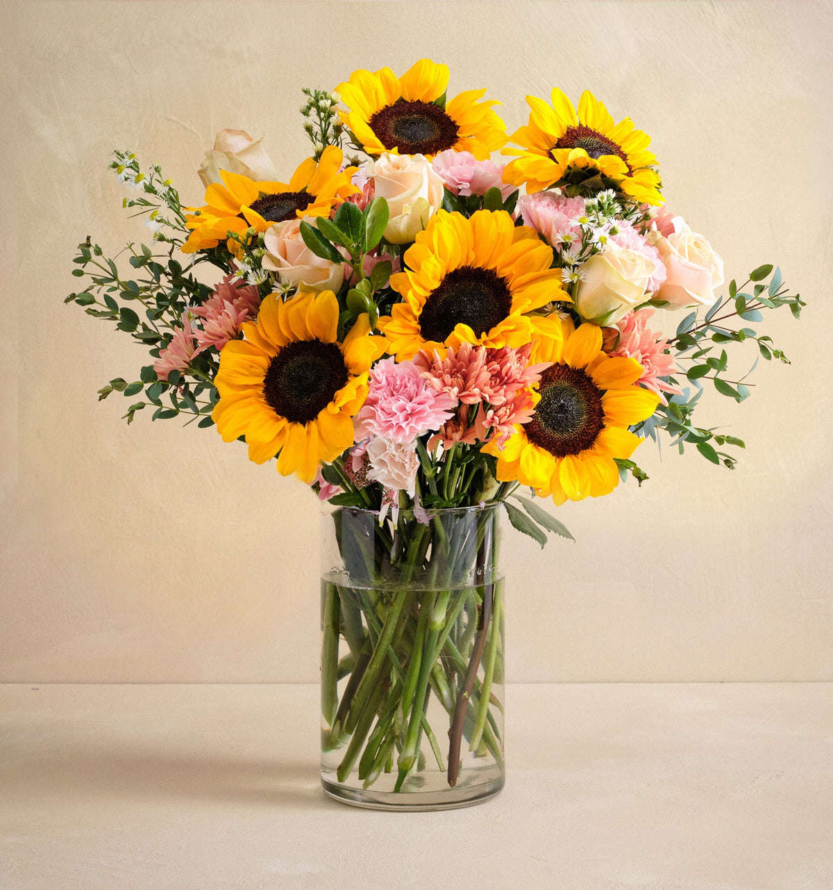 Bouquet of sunflowers and pink flowers in a clear vase on a beige background