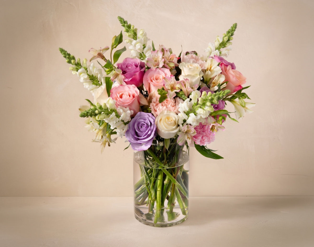 Bouquet of colorful flowers in a clear vase on a beige background