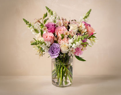 Bouquet of colorful flowers in a clear vase on a beige background