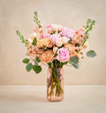 Bouquet of pink and peach flowers in a clear vase on a beige background