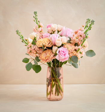 Bouquet of pink and peach flowers in a clear vase on a beige background