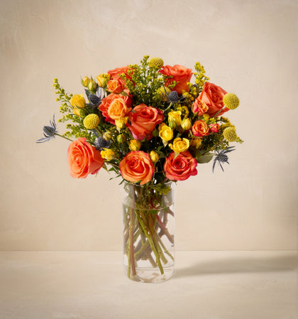 Vase with vibrant mixed flowers placed on a neutral background.