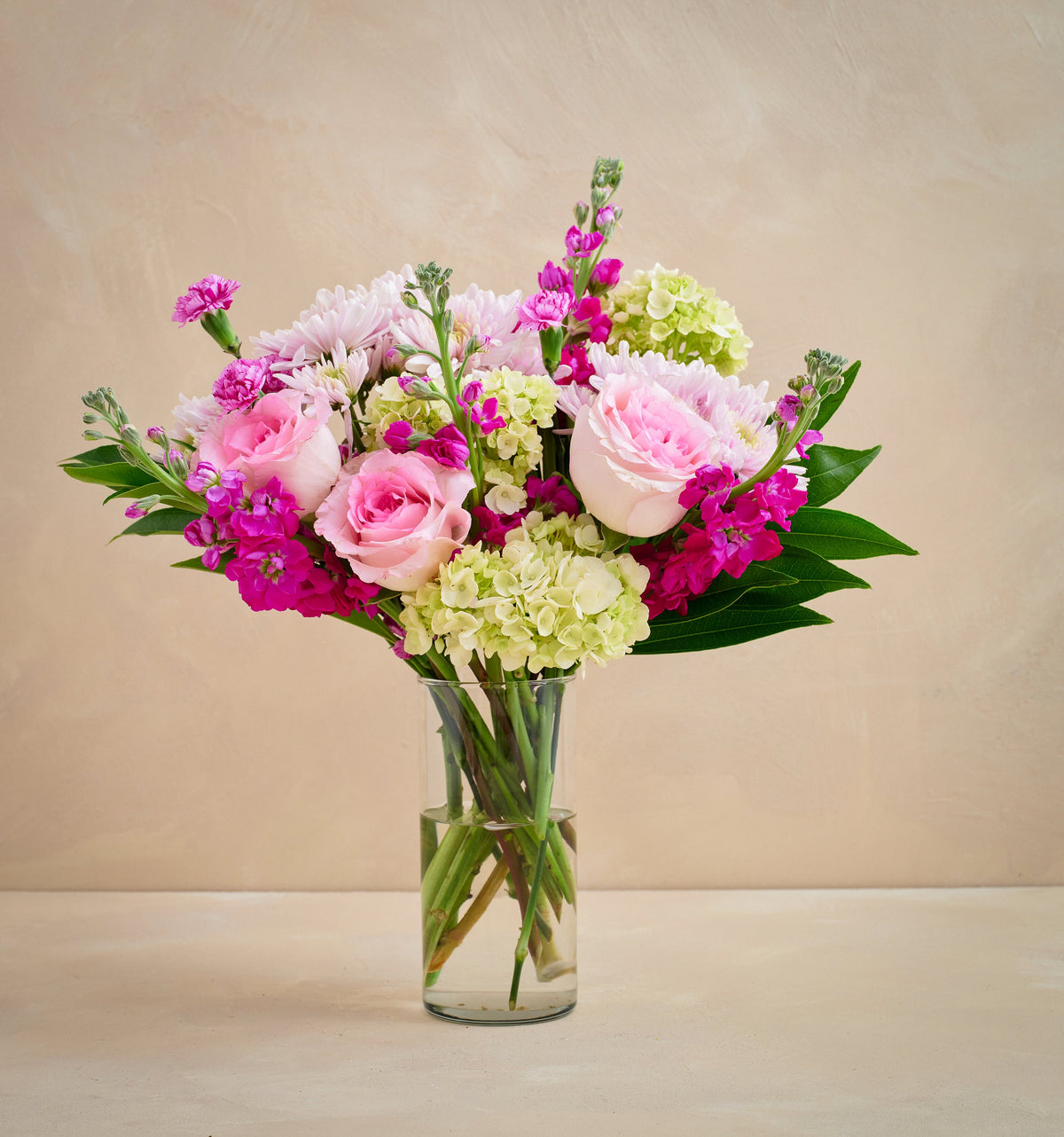 Bouquet of pink, green, and purple flowers in a clear vase on a beige background