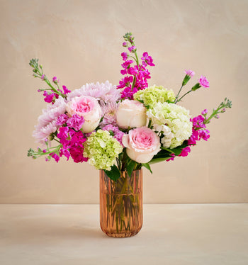 Bouquet of pink, white, and green flowers in a clear vase on a beige background