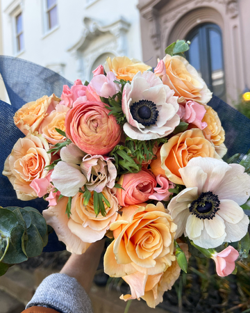 Bouquet of colorful flowers held by a person with a blurred building background