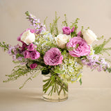 Bouquet of pink, white, and green flowers in a clear vase on a beige background