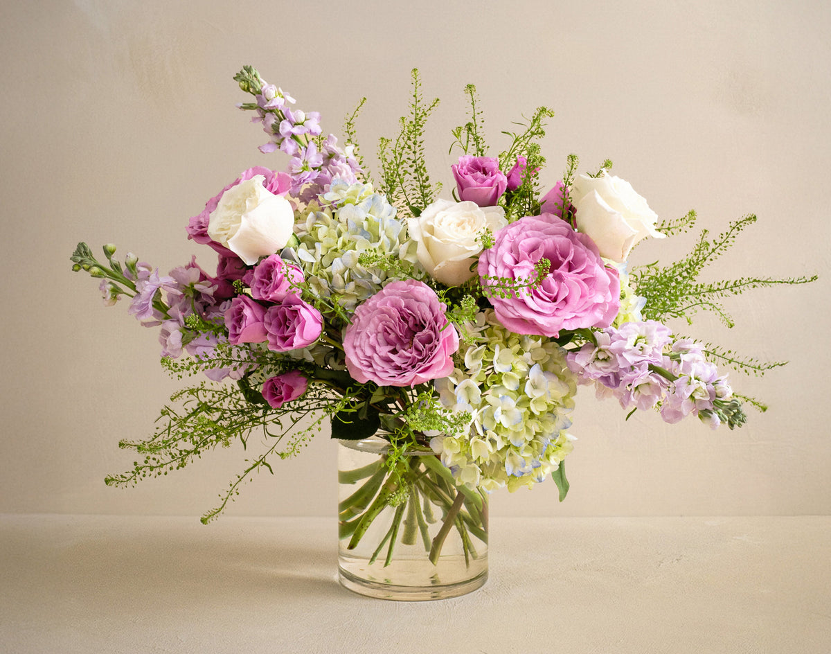 Bouquet of pink, white, and green flowers in a clear vase on a beige background