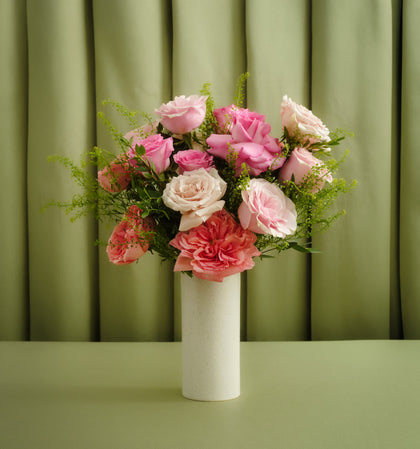 Bouquet of pink and white flowers in a white vase against a green curtain background