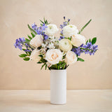 Bouquet of white and purple flowers in a white vase on a beige background