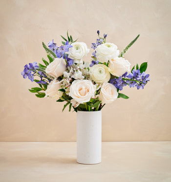 Bouquet of white and purple flowers in a white vase on a beige background