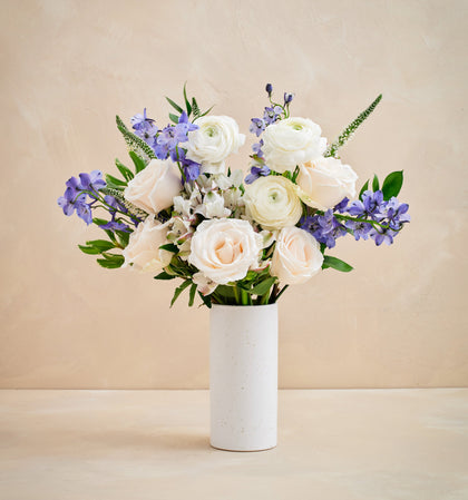 Bouquet of white and purple flowers in a white vase on a beige background