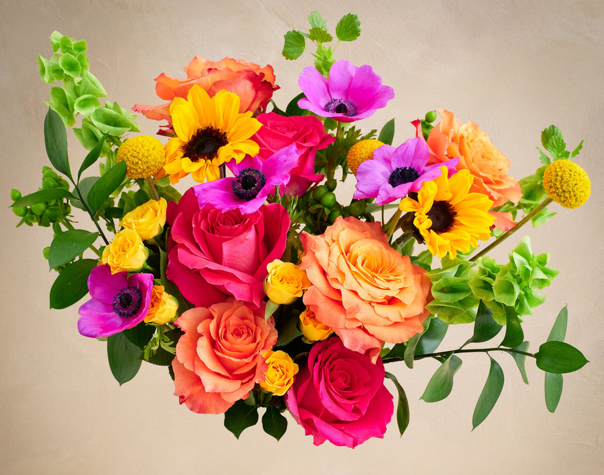 Bouquet of colorful flowers including roses and sunflowers on a beige background