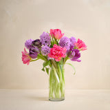Bouquet of pink and purple flowers in a clear vase on a light background