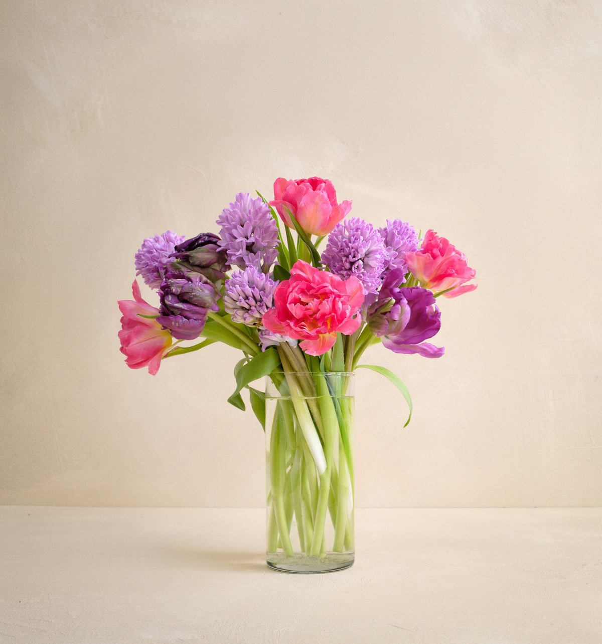 Bouquet of pink and purple flowers in a clear vase on a light background