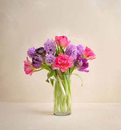 Bouquet of pink and purple flowers in a clear vase on a light background