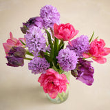 Bouquet of pink and purple flowers in a clear vase on a beige background