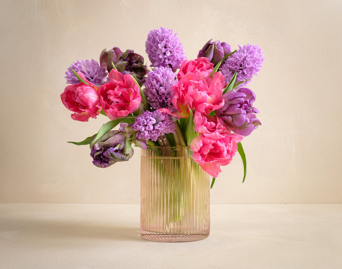 Bouquet of pink and purple flowers in a clear vase on a beige background