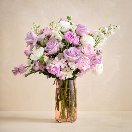 Bouquet of pink and white flowers in a clear vase on a beige background