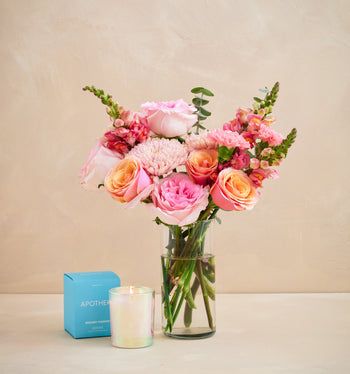 Bouquet of pink and peach flowers in a clear vase on a beige surface with a light background