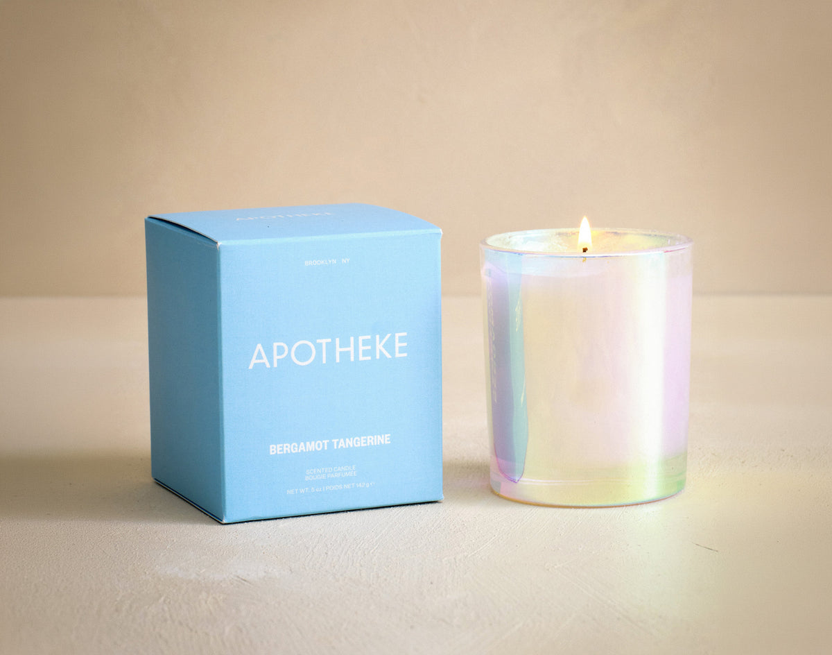 Iridescent candle next to its packaging box labeled 'Apotheke' on a beige background
