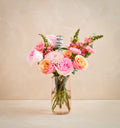 Bouquet of pink and orange flowers in a clear vase on a beige background
