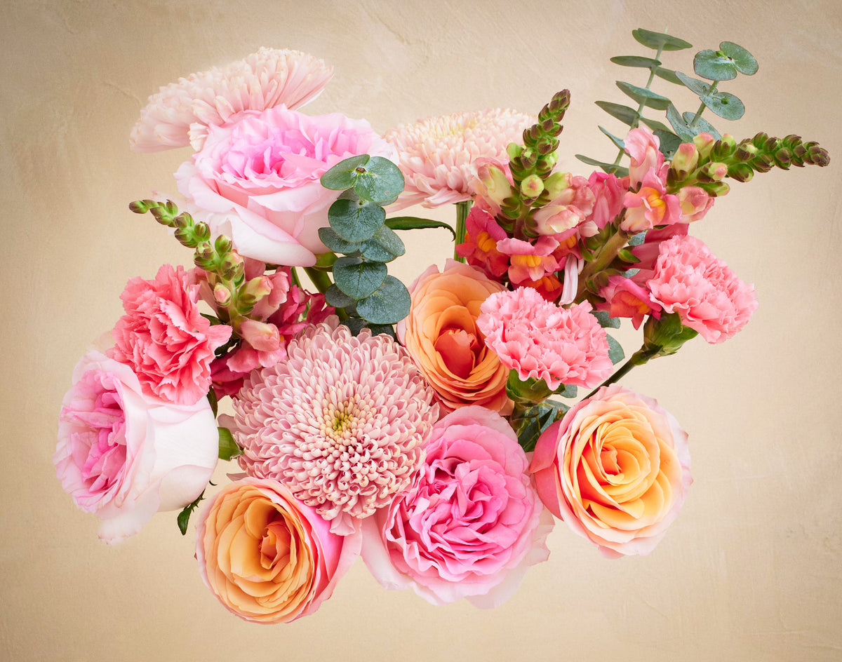 Bouquet of pink and orange flowers with green leaves on a beige background