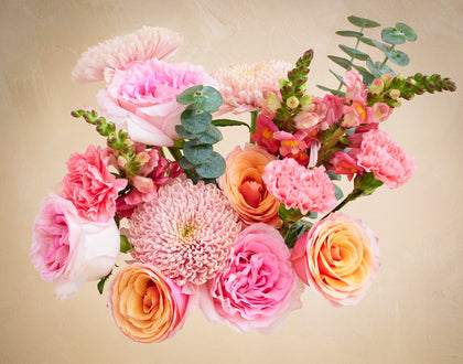 Bouquet of pink and orange flowers with green leaves on a beige background