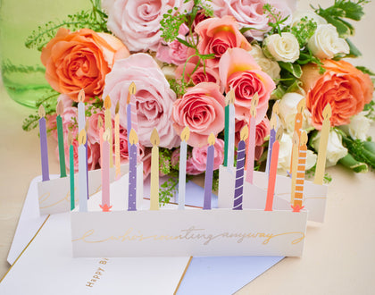 Floral arrangement with candles and a card on a light background