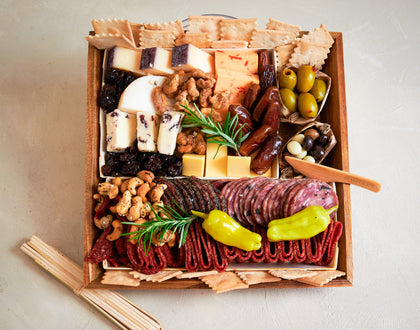 Assorted meats, cheeses, and snacks in a wooden box on a light background