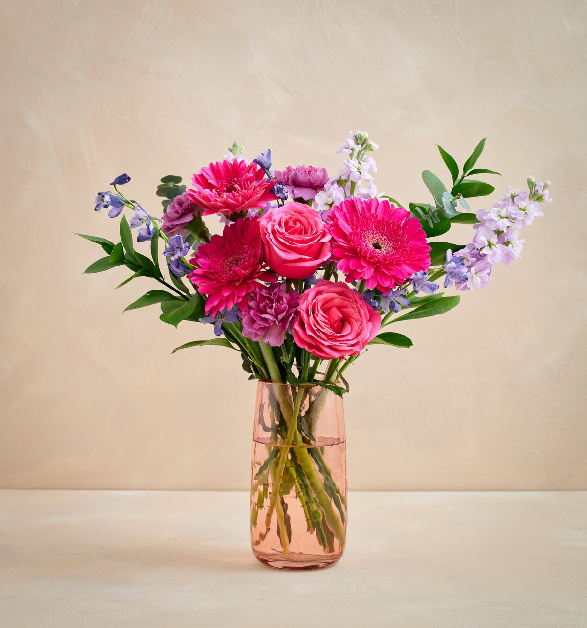 Bouquet of pink and purple flowers in a clear vase on a beige background