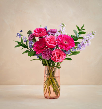 Bouquet of pink and purple flowers in a clear vase on a beige background